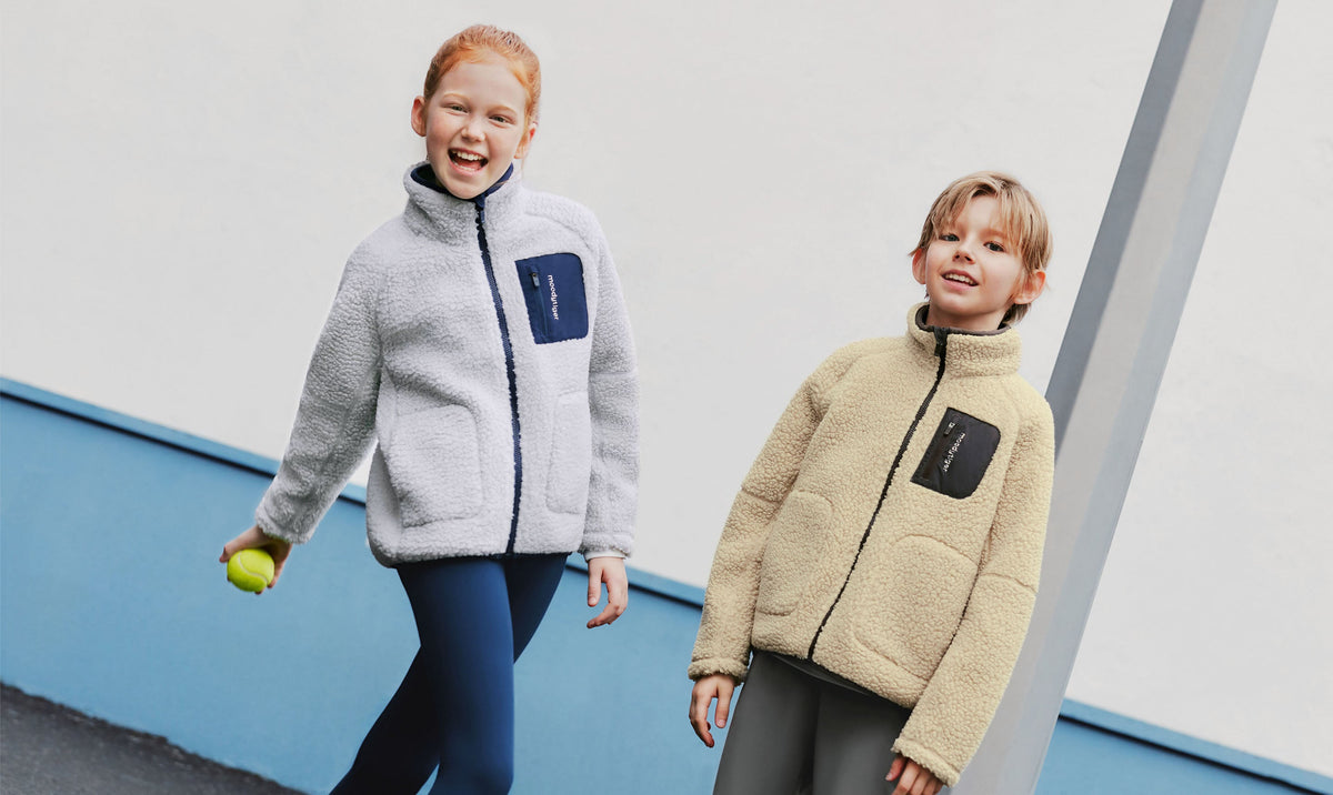 Two kids in grey and cream sherpa fleece jackets walking outdoors
