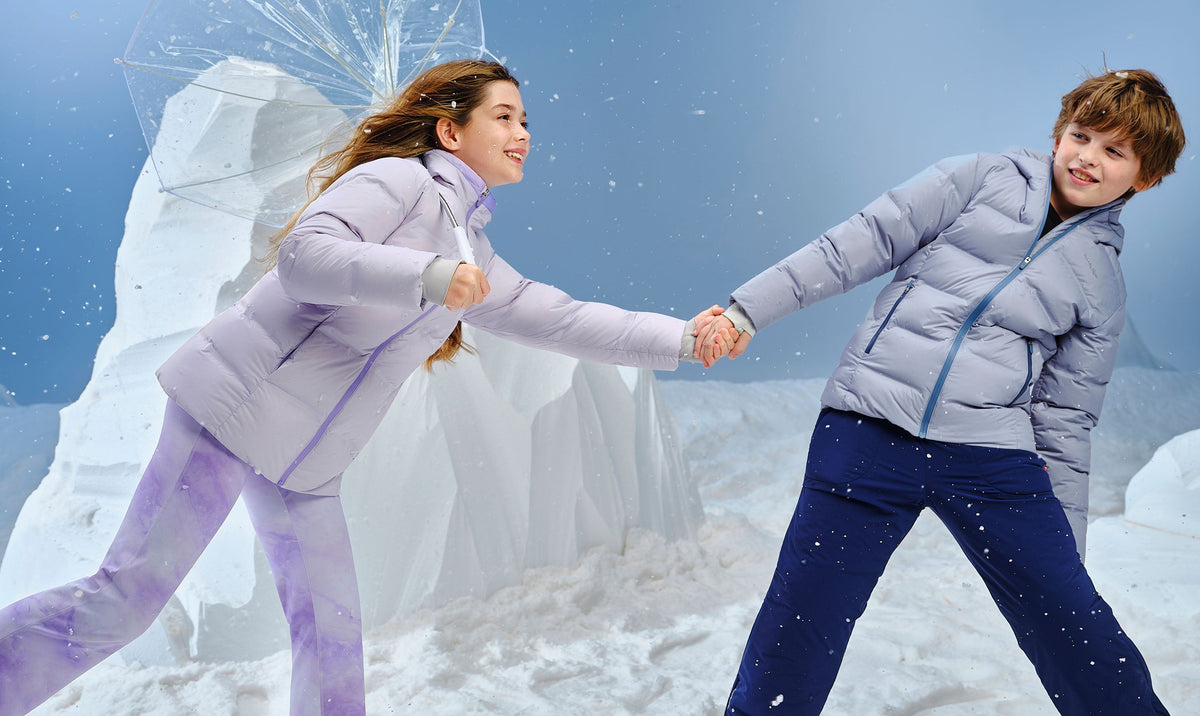 Girl and boy in light quilted down jackets holding hands and playing in falling snow