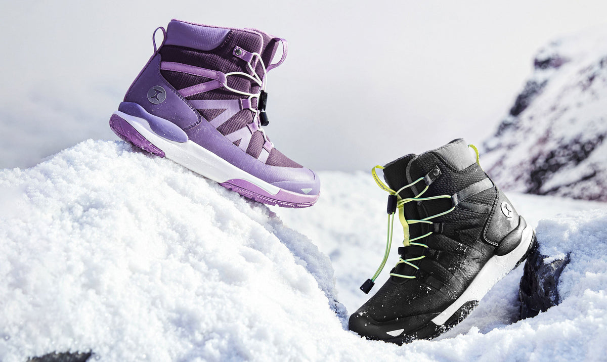 Purple and black kids' winter boots with quick-pull laces resting on fresh snow